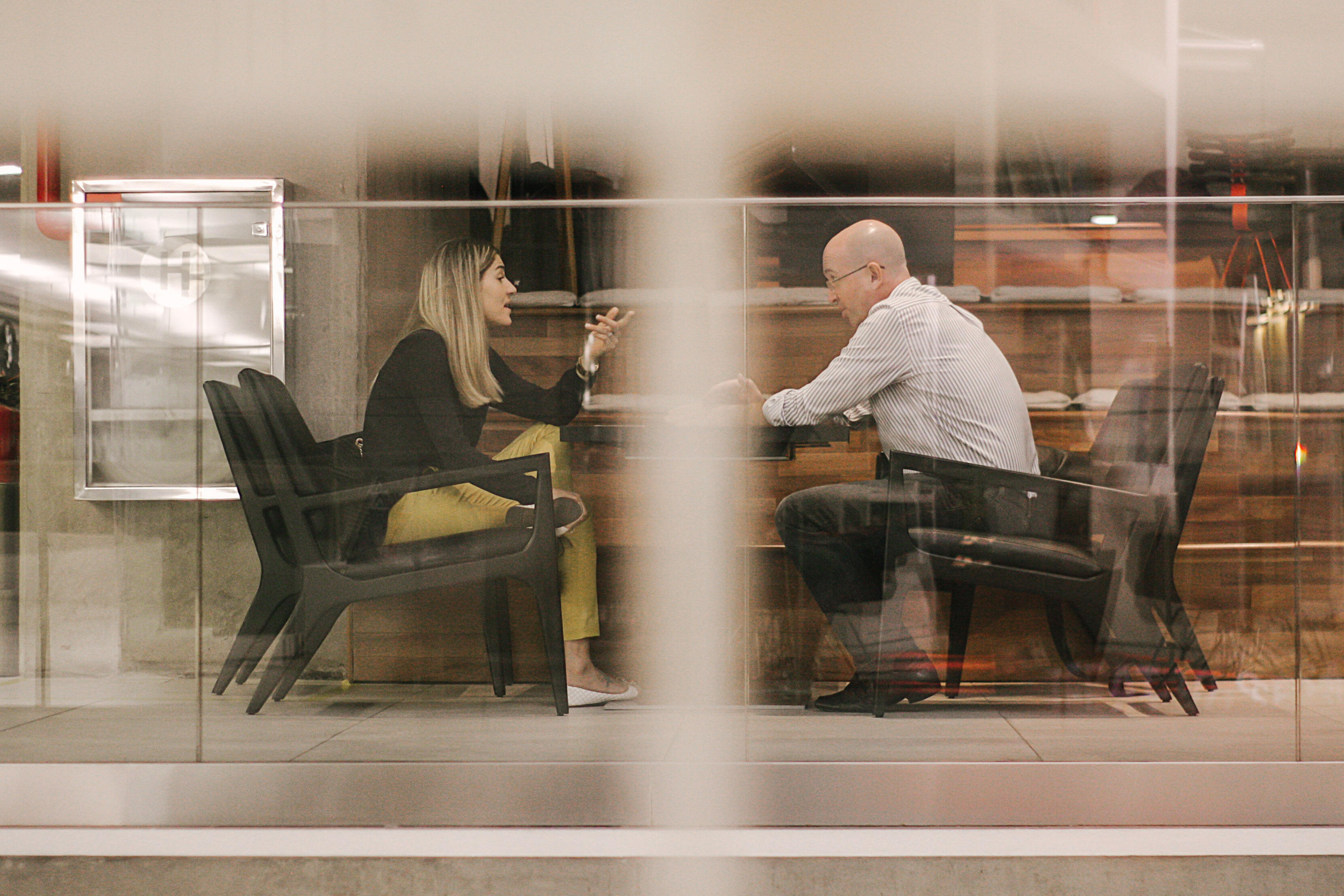 female and male sitting in office lounge chairs having a quiet work conversation